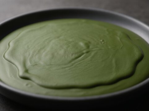 Creamy Green Soup Close-up: A bowl of vibrant green, creamy soup, possibly a vegetable or herb blend, presented in a dark, minimalist bowl, inviting with its smooth texture and rich color.