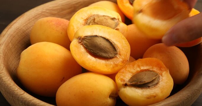 Woman putting halves of fresh apricot into bowl with fruits, closeup
