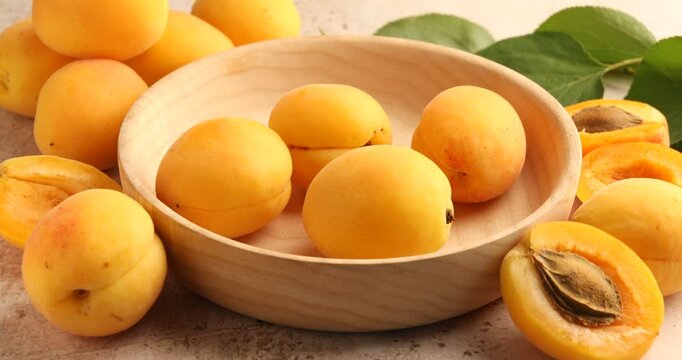 Woman putting fresh apricots into bowl at textured table, closeup