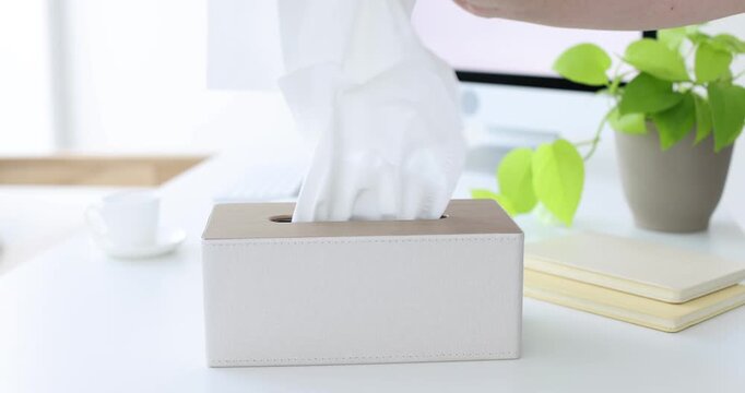 Woman taking paper tissues out of holder at white desk, closeup