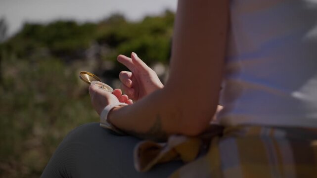Woman holding a golden retro compass in her hands, checking the direction for navigation during a nature hike, symbolizing adventure, exploration, and finding the right path