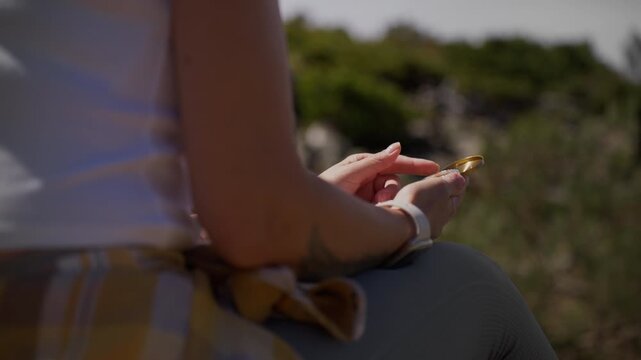 Close-up of a female hiker's hands opening a classic golden compass to find her way. The woman is resting outdoors, using the navigational tool to check her direction and orient herself