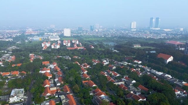Aerial view of a hazy city skyline with residential houses and green trees at dawn.