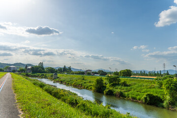 Obraz premium Rural River Landscape with Green Banks Under a Bright Blue Sky
