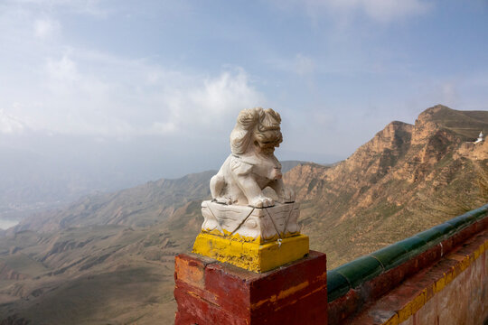 A stone lion statue overlooks the mountains from a wall at Shachong monastery, Qinghai Province, Wayaotai, China