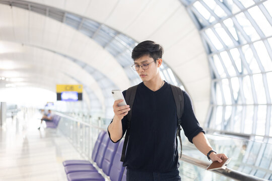 close up young asian man smile and looking while holding passport ,ticket and smartphone in airport departure area for traveling and people lifestyle concept