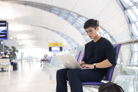 close up young asian businessman use smartphone to check about email or notification from social media while sitting for waiting boarding time in the airport and working on laptop for business travel