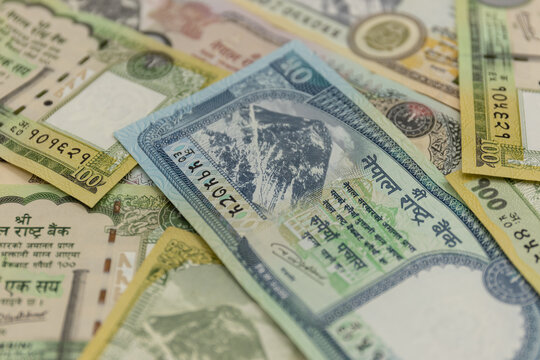 Nepalese rupee and United States dollar banknotes arranged together as physical paper currencies, displaying the distinctive colors, denominations, portraits, national symbols, architectural elements