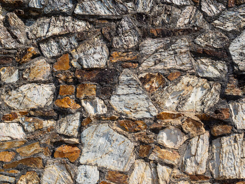 Close-up design texture showing a colourful section of wall constructed with irregular pieces of stone and rock of different sizes.