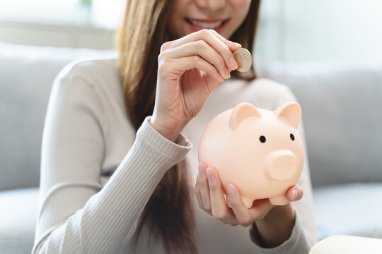 Young woman saving money monthly expenses putting coin in to piggy bank on the table.