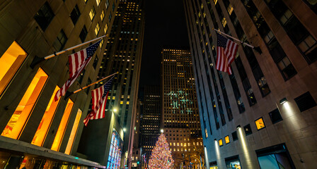 Obraz premium Christmas tree in NYC glowing during winter night. Winter holiday in New York festive city scene. New York winter atmosphere with Christmas decorations. New York City Christmas season downtown.