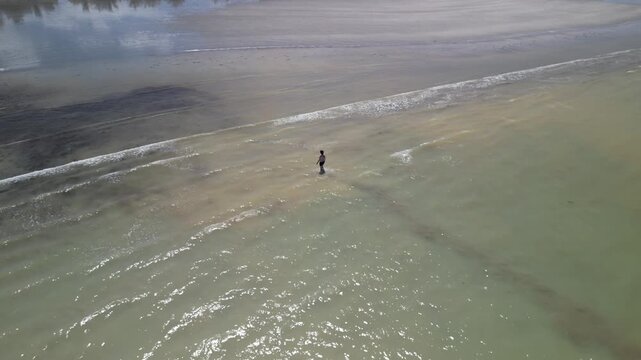 Vista a&eacute;rea de pessoa solit&aacute;ria caminhando em praia extensa na mar&eacute; baixa, cena de introspec&ccedil;&atilde;o durante viagem tranquila ao litoral