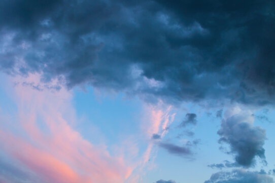 Picturesque sky background. Soft pink and blue clouds at dusk. A gradient sky with gentle pastel tones and a dark cloud mass