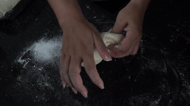 Close up of hands pressing and kneading homemade dough on a floured work surface during bread making.