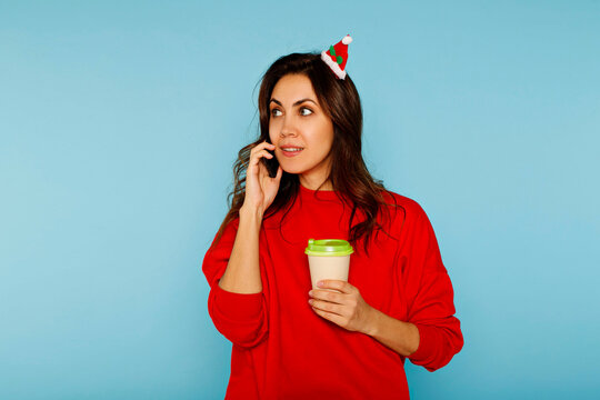 Woman talking on phone holding coffee wearing christmas hat