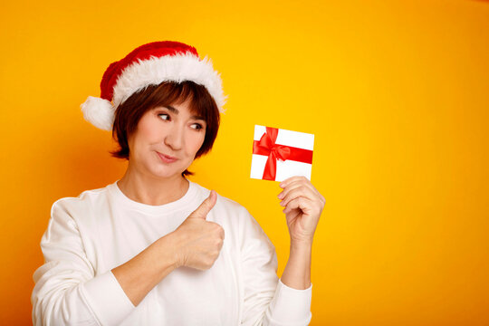 Woman wearing santa hat holding gift card giving thumbs up