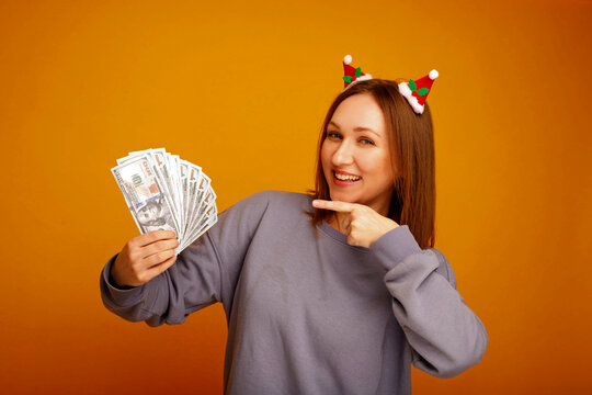 Woman wearing christmas head band holding dollar bills pointing