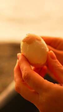 Egg peeling hands person carefully removes the shell from a hard-boiled egg on a sandy beach during a warm golden hour sunset
