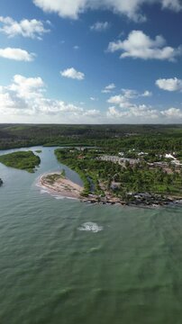 Vista a&eacute;rea de vilarejo costeiro &agrave; beira de rio que des&aacute;gua no mar, paisagem serena de encontro entre &aacute;gua doce e salgada durante viagem pelo litoral