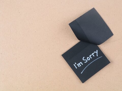 Black adhesive note with handwritten white text I'm sorry placed on a textured brown background. Ideal for apology concepts, regret, forgiveness, and emotional relationship design projects