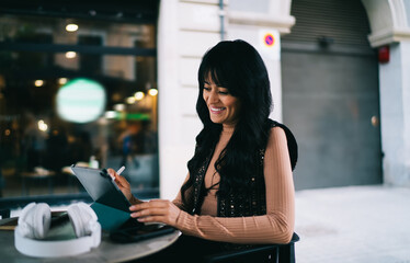 Joyful Caucasian female student operating digital tablet with stylus pen at outdoor terrace table, checking e-commerce retail app product deliveries order status and online store sales © BullRun