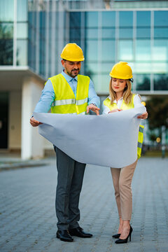 Two engineers reviewing construction plans outside a modern office building