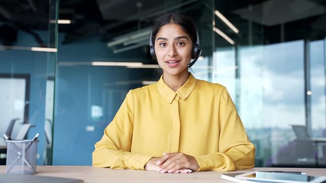 Webcam view of young businesswoman in wireless headset looking at camera while talking on video call. Female coach or tutor conducting online course, webinar, or virtual training session from office.