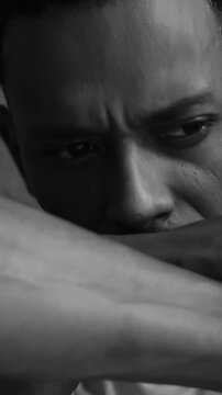 African American man sitting against wall looking down in deep thought and sadness