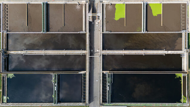 Aerial view of a wastewater treatment plant with large rectangular sedimentation tanks, industrial pipes, and water filtration systems in Marche, Italy.
