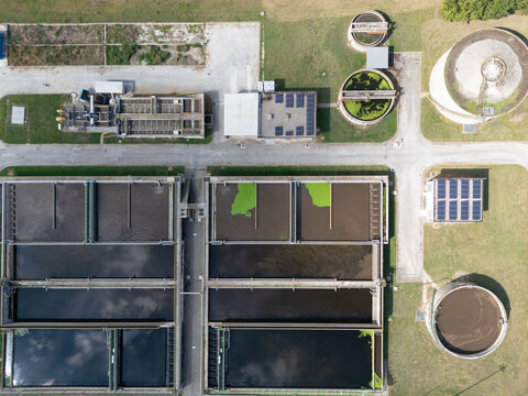 Aerial view of a wastewater treatment plant with sedimentation tanks, filtration basins, and circular clarifiers surrounded by green grass in Marche, Italy.