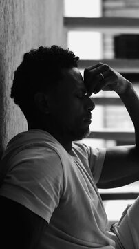 African American man sitting on ground against wall with arms stretched forward in black and white