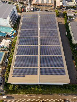 Aerial view of a large industrial warehouse roof covered with extensive solar panel arrays in the Zama industrial area, Zama, Kanagawa, Japan.