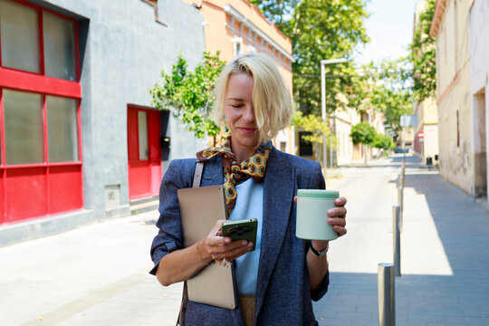 Woman Walking on Street While Using Phone and Holding a Cup