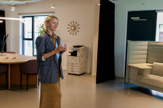Woman Stands in Modern Office Holding a Drink While Smiling