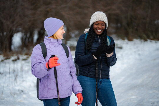 Two diverse women enjoying a winter hike on a snowy trail, laughing and smiling