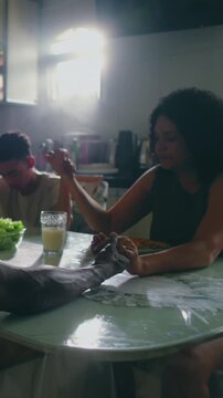 Hispanic family holding hands in prayer before meal at dining room table indoors