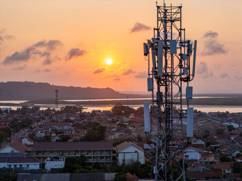 Aerial view of a telecommunications tower standing over the residential rooftops of the coastal city during a vibrant sunset. Cilacap, Central Java, Indonesia.