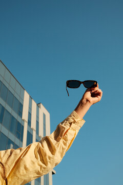 Close up photo of female hand holding sunglasses opposite blue sky