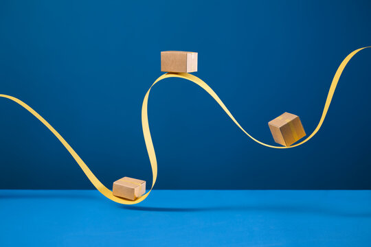 Cardboard boxes precariously balanced on a wavy yellow ribbon