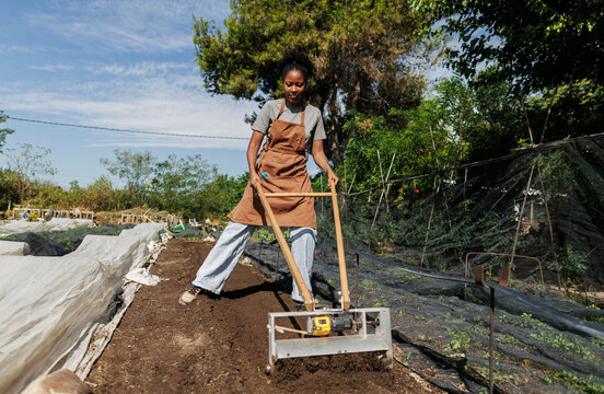 Young woman cultivating soil with a hand tiller in organic garden