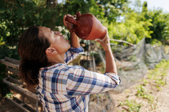 Woman drinking water from traditional clay pitcher outdoors