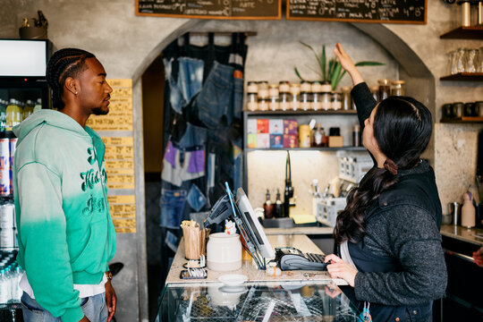 Customer Choosing from Menu at Cafe Counter with Barista