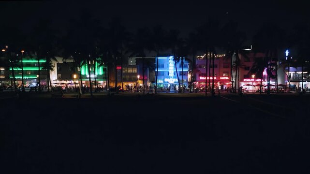 Vibrant neon towers illuminate Collins Avenue in sweeping aerial footage