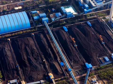 Aerial view of a large industrial coal storage facility with conveyor belts and blue-roofed buildings in Indonesia.