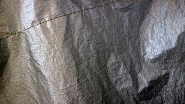 Silver plastic tarp texture creating abstract crumpled reflections and material background