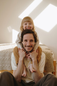 Happy father hugging his laughing toddler son from behind at home