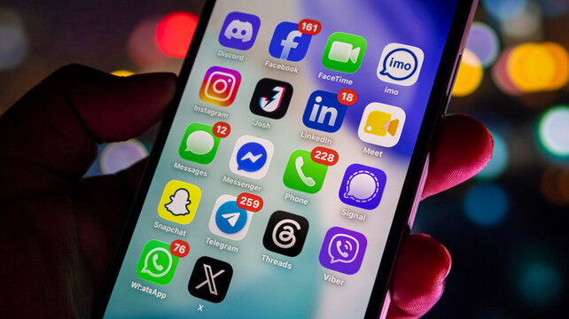 Social media and messaging app icons on smartphone screen with notification badges in evening light.