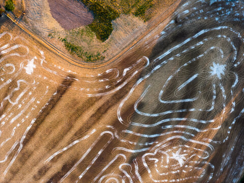 Aerial view of intricate white tire track patterns etched into a dry agricultural field in Hook, England, United Kingdom.