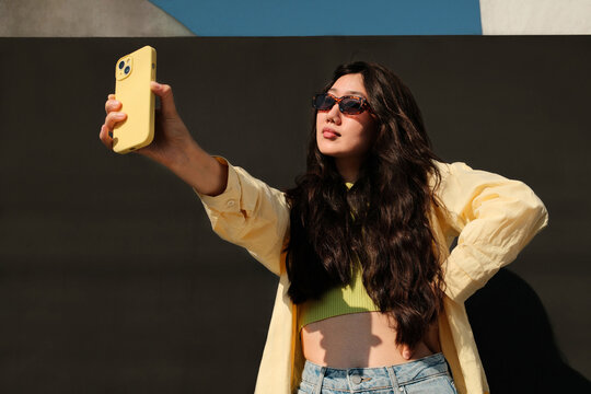 Portrait of stylish asian woman in sunglasses making selfie with phone