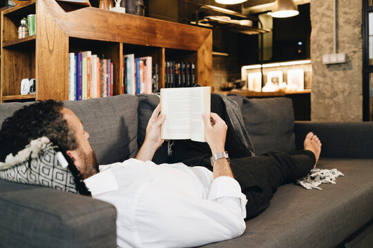 Person relaxing reading book on comfortable couch at home